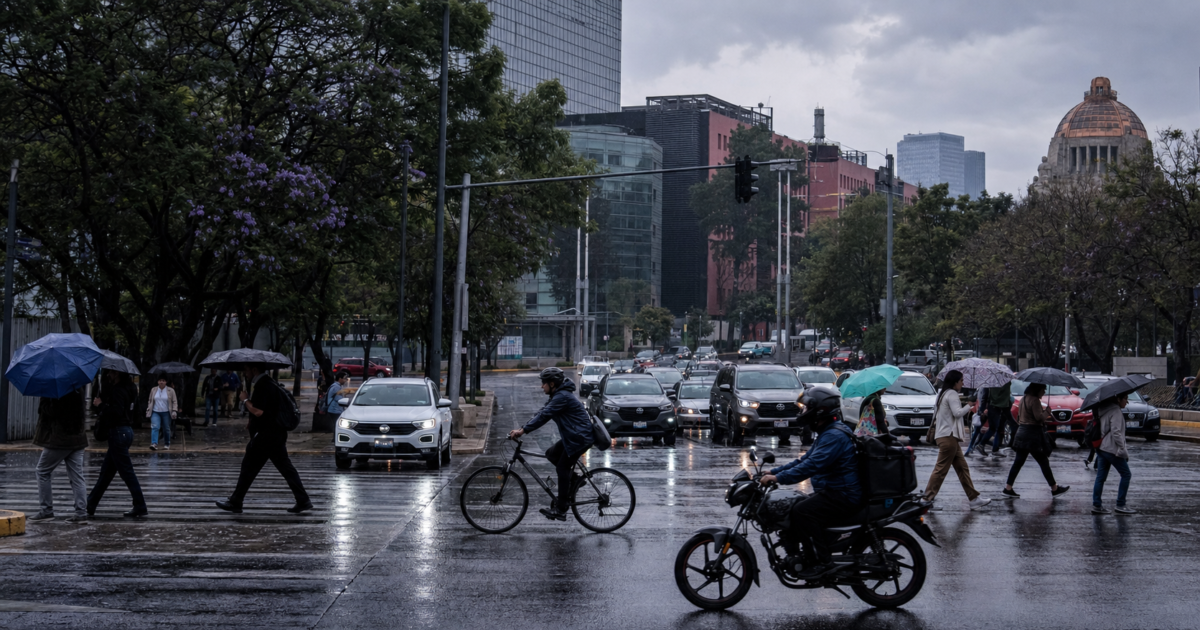 Automóviles avanzan lentamente sobre una avenida de la Ciudad de México mientras peatones cruzan con paraguas bajo un cielo nublado; al fondo se observan señales viales y edificios urbanos.