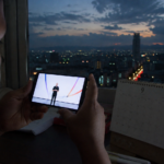 Persona observa una transmisión tecnológica en su teléfono junto a un calendario con el número 9, con la ciudad de México al anochecer.