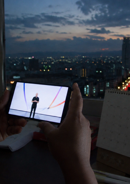 Persona observa una transmisión tecnológica en su teléfono junto a un calendario con el número 9, con la ciudad de México al anochecer.