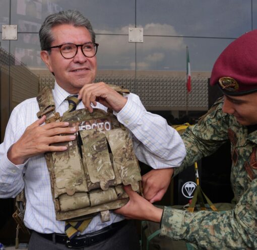 Ricardo Monreal ajusta un chaleco táctico con ayuda de un militar durante una exhibición.