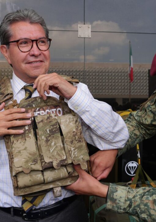 Ricardo Monreal ajusta un chaleco táctico con ayuda de un militar durante una exhibición.