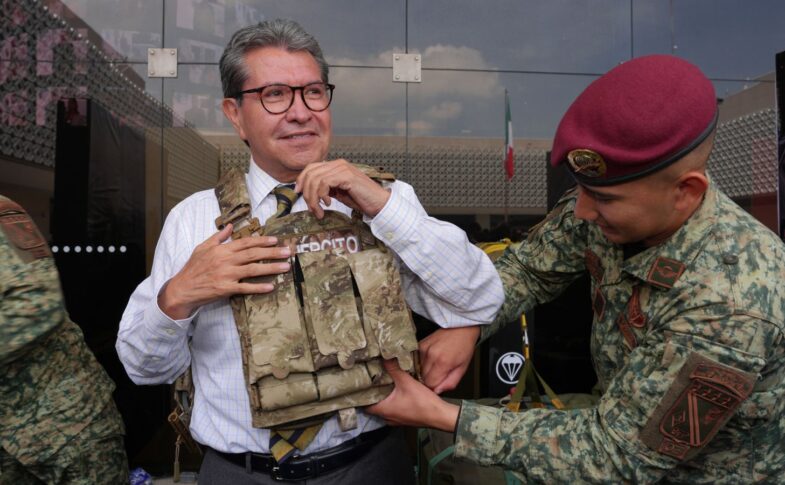 Ricardo Monreal ajusta un chaleco táctico con ayuda de un militar durante una exhibición.