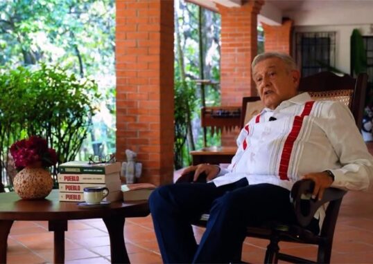 Andrés Manuel López Obrador sentado junto a varios ejemplares de su libro Pueblo