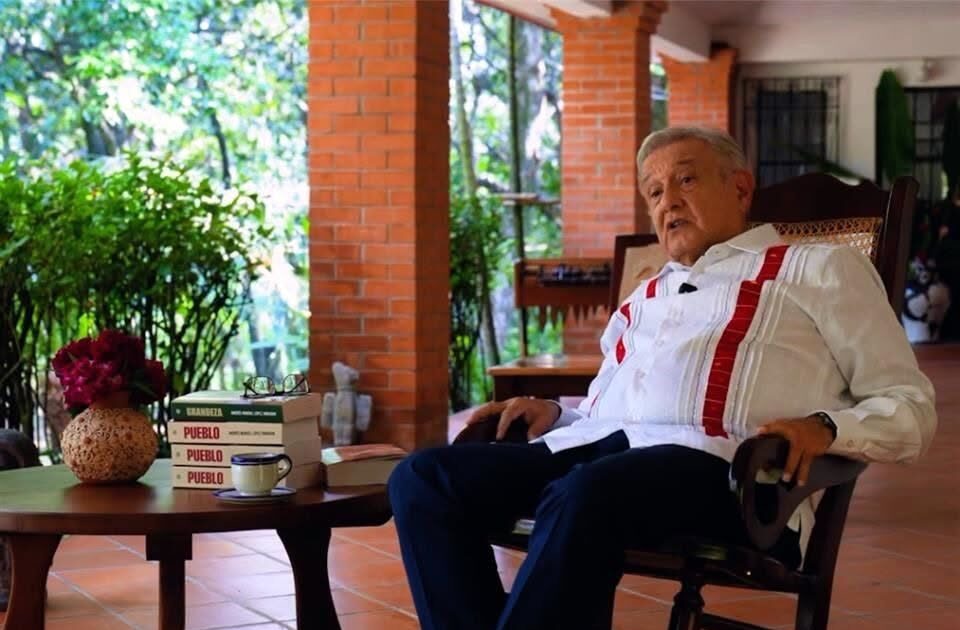 Andrés Manuel López Obrador sentado junto a varios ejemplares de su libro Pueblo