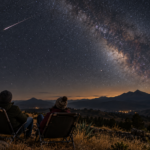 Personas observando un cielo nocturno con una estela de meteoro sobre montañas; ilustración generada con IA.
